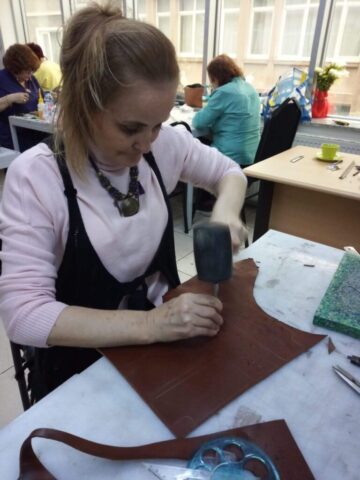 Katılımcının yoğun bir dikkatle çalıştığı bu kare, atölye eğitimlerimizin uygulamalı yönünü en iyi şekilde yansıtıyor. Deri üzerine şekil verme ve işleme aşamasında kullanılan çekiçle, el emeğiyle üretim süreci titizlikle yürütülüyor. Arka plandaki diğer katılımcılar da aynı özenle çalışmalarına devam ediyor, bu da atölyemizin üretken ve odaklı atmosferini ortaya koyuyor.