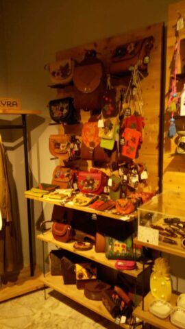 Bu stand görseli, el emeği göz nuru deri çanta ve aksesuarların sergilendiği şık ve dikkat çekici bir düzenlemeye sahip. Dikey ahşap panel üzerine yerleştirilmiş farklı boyut ve tarzlarda çantalar, özellikle çiçek motifleriyle süslenmiş modellerle estetik bir bütünlük oluşturuyor. Standın alt raflarında cüzdan ve daha küçük çanta çeşitleri yer alırken, üst bölümler askılı çantalarla zenginleştirilmiş. Renk ve model çeşitliliği, ziyaretçilere el işçiliğinin zarafetini ve ürünlerin özgünlüğünü açıkça yansıtıyor. Fuar ve sergi alanlarında markanın özgün karakterini yansıtan bu tür sunumlar, ziyaretçilerin ilgisini çekmede oldukça etkili olur.