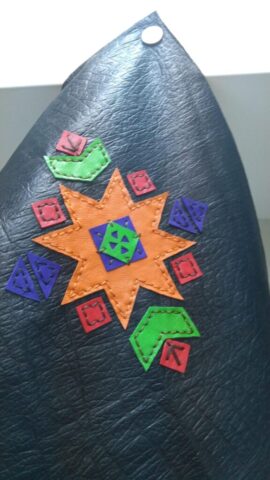 Bu göz alıcı motif, Anadolu kültüründe güneşin yaşam veren gücünü simgeleyen yıldız formundan ilham alır. Ortadaki yeşil sekizgen form, bereket ve dengeyi temsil ederken, etrafındaki turuncu yıldız yaşam enerjisini ve ışığı sembolize eder. Kırmızı kareler ve mor üçgenler geçmişin izlerini, köklerimizi ve geleneksel estetiği yansıtır. Yeşil köşeler doğayla olan bağı simgeler. Tamamı doğal deriden kesilen parçalar tek tek elde dikilmiş, renkli kombinasyonuyla modern ve dinamik bir görünüm elde edilmiştir. Bu motif; çanta kapakları, duvar panoları veya özel deri aksesuarlar için kültürel anlam taşıyan özgün bir tasarımdır.