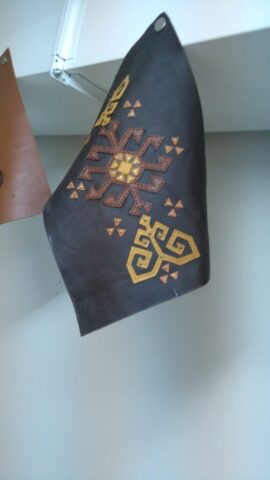 Bu motif, kadim Anadolu uygarlıklarının güneş ve yaşam döngüsü sembollerinden ilham alır. Ortadaki dairesel yapı, enerjiyi ve hayatı simgelerken etrafındaki kollar ışığın dört bir yana yayılışını anlatır. Köşelerdeki geometrik sarı motifler ise “koç boynuzu” figüründen esinlenilmiştir – bu figür cesareti, direnci ve bereketi temsil eder. Her bir parça elde kesilmiş, deri üzerine tek tek yerleştirilerek geleneksel tekniklerle işlenmiştir. Modern tasarımı ve kültürel kökleri bir arada taşıyan bu motif, çanta, cüzdan ya da dekoratif ürünlerde dikkat çekici bir odak noktası yaratır.