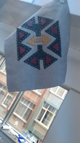 Bu özgün tasarım, dört yöne açılan yolları ve evrensel denge arayışını simgeliyor. Ortadaki ok formundaki geometrik detay, karar ve yön belirleme anlamı taşırken; çevresindeki üçgenler hareketi, dönüşümü ve çoklu bakış açısını temsil eder. Hakiki deriden el işçiliğiyle kesilen parçalar, geleneksel Türk motiflerinden esinlenerek modern bir yorumla bir araya getirilmiştir. Koyu lacivertin derinliği, hardal ve bordo tonlarının enerjisiyle dengelenmiştir. Bu motif, özellikle sırt çantası, el çantası ya da deri cüzdanlarda güçlü bir görsel imza bırakır.