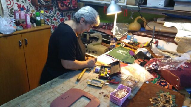 Atölyemizde her ürün, bir ustanın ellerinde hayat bulur. Bu karede, katılımcımız yoğun dikkat ve incelik gerektiren bir detay çalışması yürütüyor. Deri kesiminden süsleme aşamasına kadar her adımda, ustalıkla yoğrulmuş bilgi ve tecrübe devrede. Modern teknikleri, geleneksel üretim anlayışıyla harmanladığımız bu ortamda; ürünlerimiz sadece estetik değil, aynı zamanda anlam yüklüdür. Her biri, el emeğinin ve tasarım ruhunun özgün bir parçasıdır.