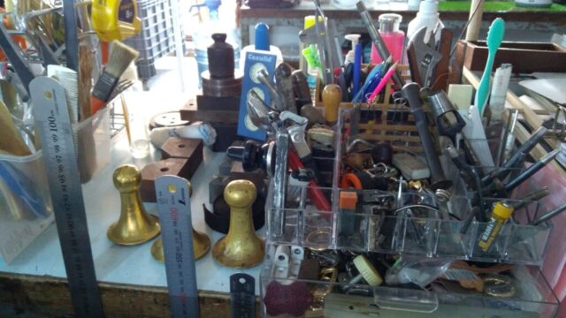 Deri atölyemizin kalbinde yer alan araç-gereç düzenini görüyorsunuz. Her bir parça, zanaatkârın işini kolaylaştıran vazgeçilmez bir yardımcıdır. Cetvelden kaleme, penseden zımba aparatına kadar çeşitlenen bu araçlar; ürünlerimizin hassas ölçülerle ve kusursuz detaylarla hazırlanmasını sağlar.